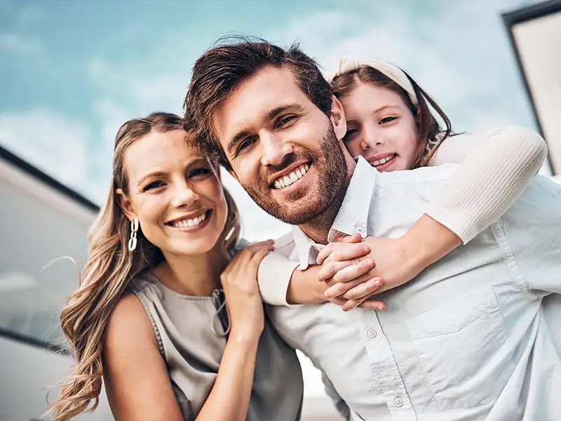 mother and father smiling with daughter outdoors under blue sky