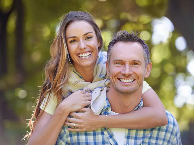 adult man and woman smiling together outdoors near trees