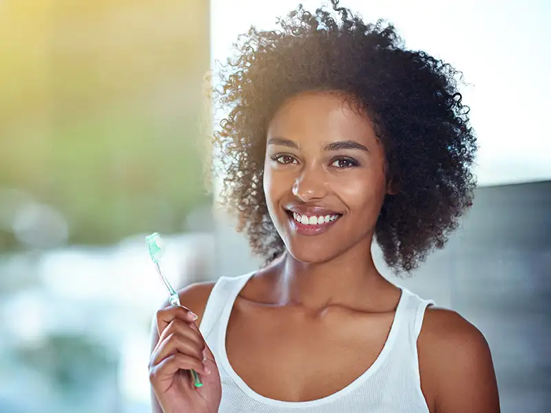 young woman smiling at home while holding toothbrush