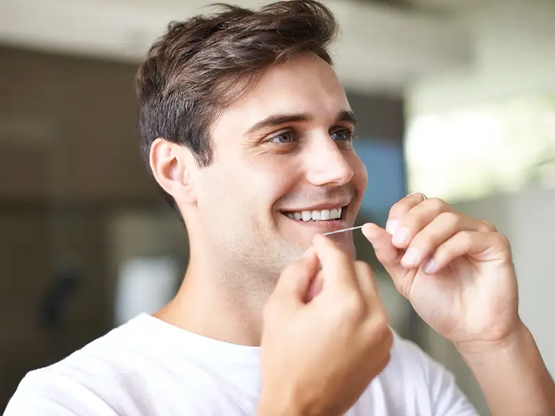 young man smiling at home preparing to floss