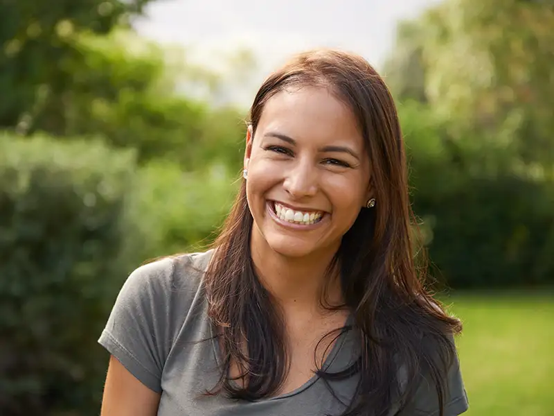 young woman smiling outdoors near trees