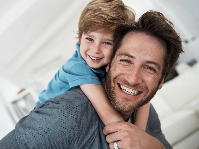father smiling with son riding on his back at home
