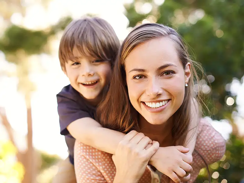mother smiling with son riding on her back outdoors