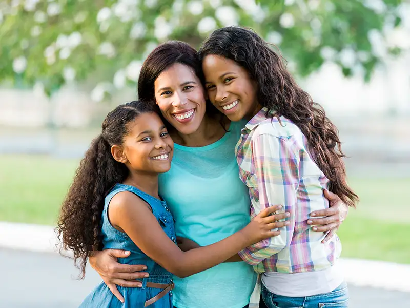 mother smiling with two daughters in the park