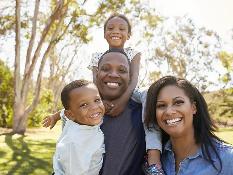 mother and father smiling together with son and daughter outdoors near trees