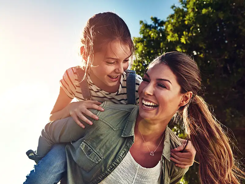 mother smiling with daughter riding on back outdoors