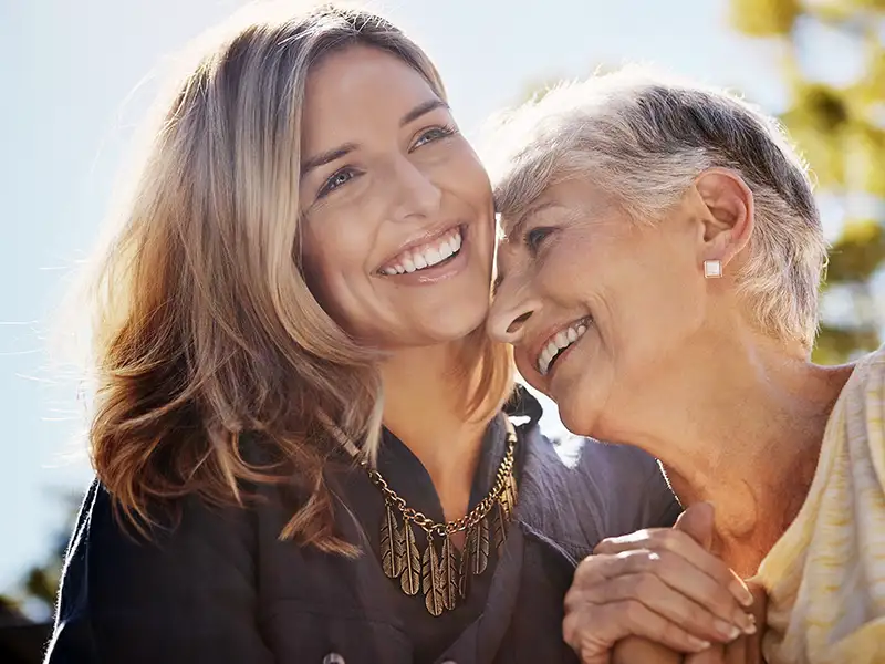adult woman smiling together with senior mother outdoors