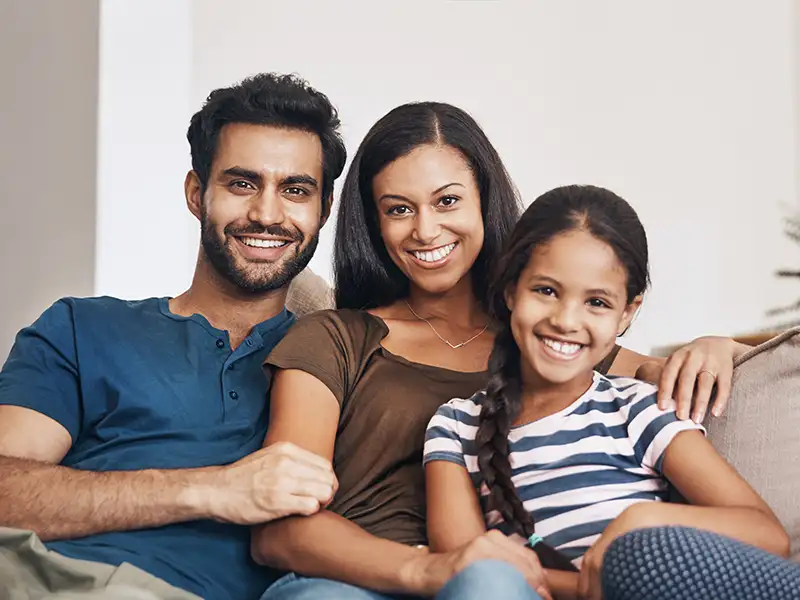mother and father smiling at home with daughter on couch