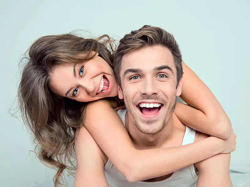 woman hanging over shoulders of man while they both smile