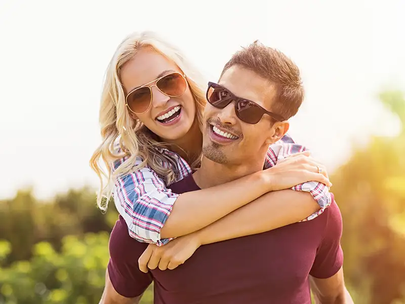 young man and woman smiling while they both wear sunglasses outdoors