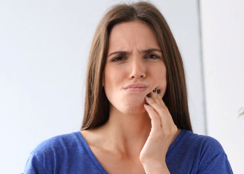 woman holding hand up to face and grimacing from tooth pain