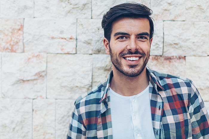 adult man smiling outdoors by white brick wall