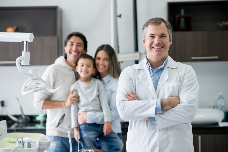 dentist smiling in the office with happy family in the background