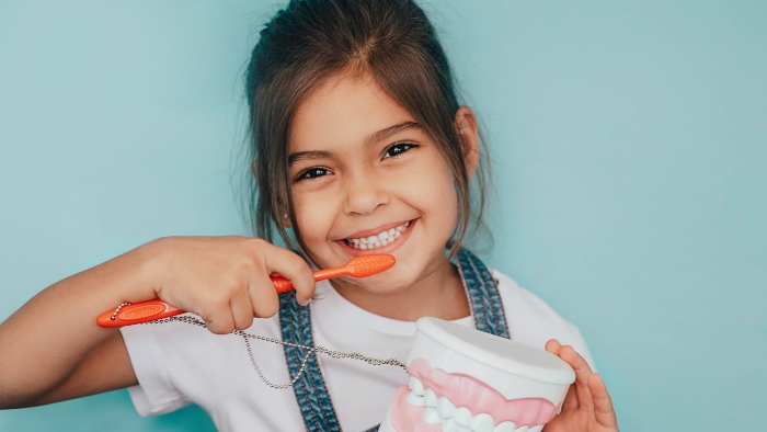 young girl smiling with toothbrush held up to mouth