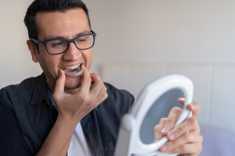 man removing night guard from mouth while holding mirror