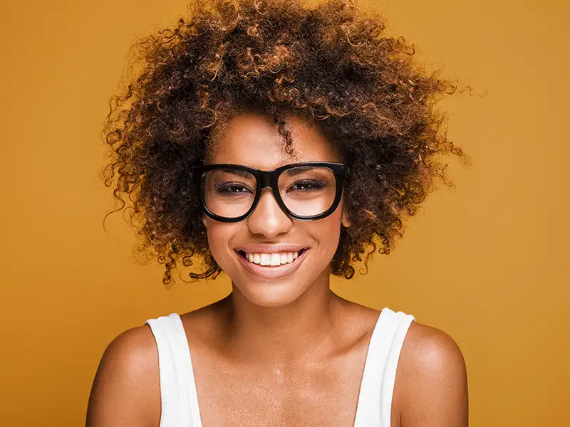 woman with glasses smiling in front of orange wall